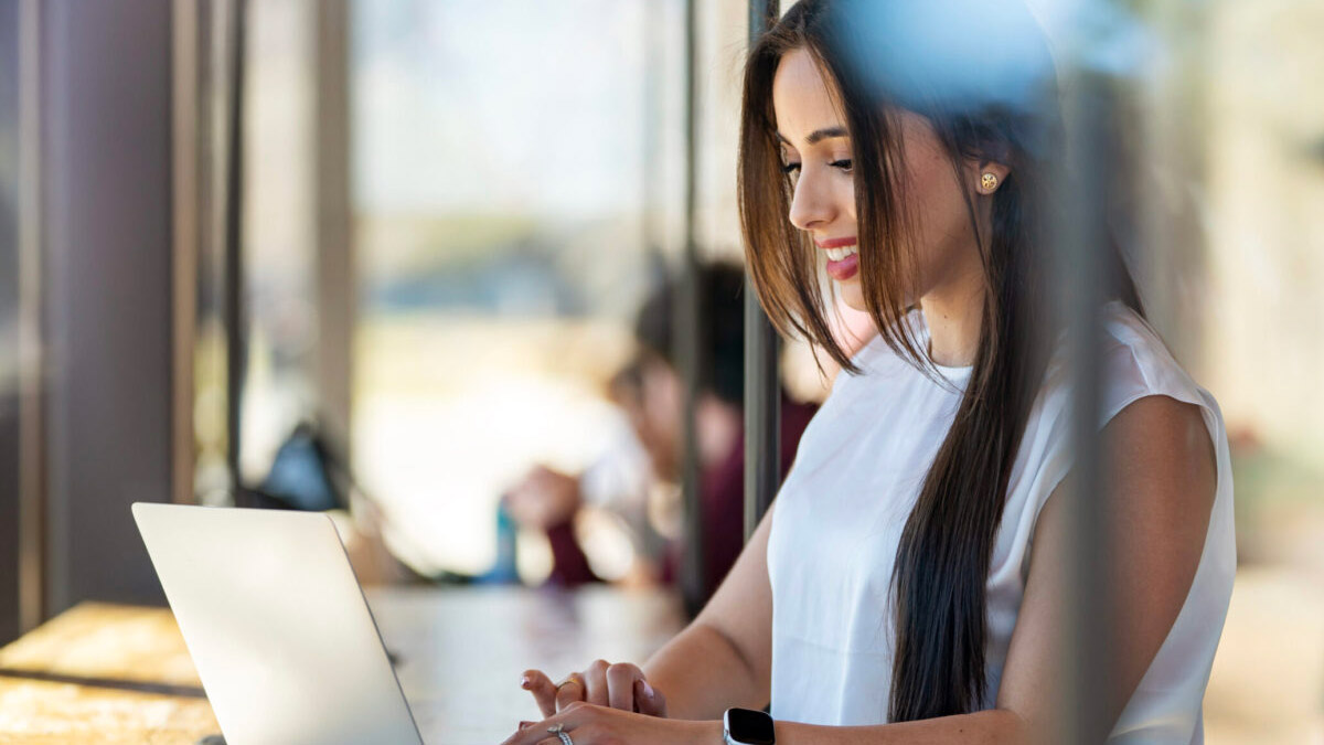 A Mays Business School student working on her laptop beside a window